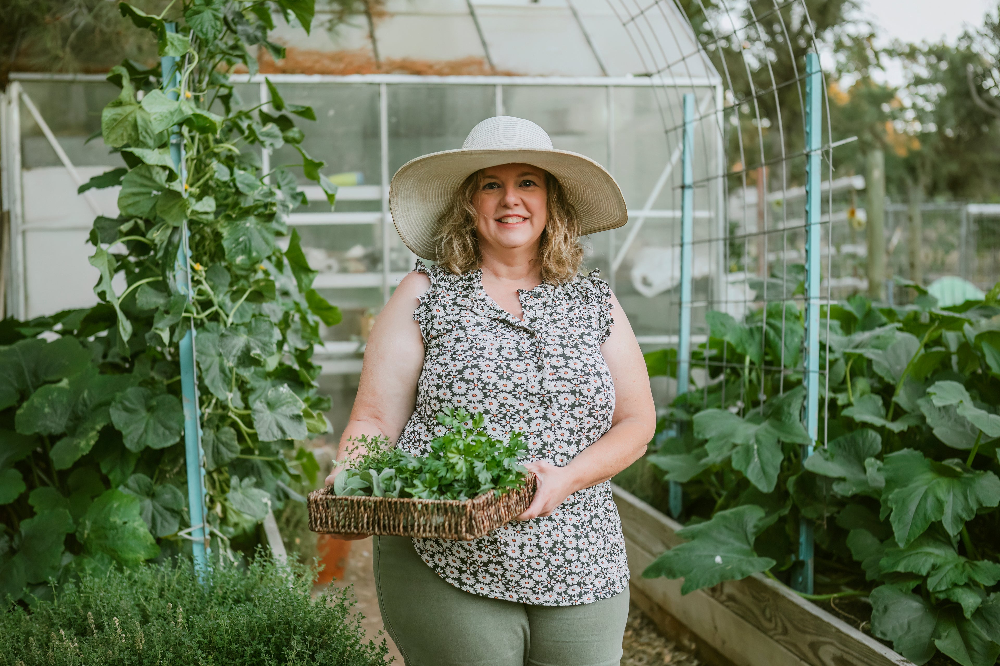 portrait of the owner in her garden holding a basket of herbs and wearing a straw hat