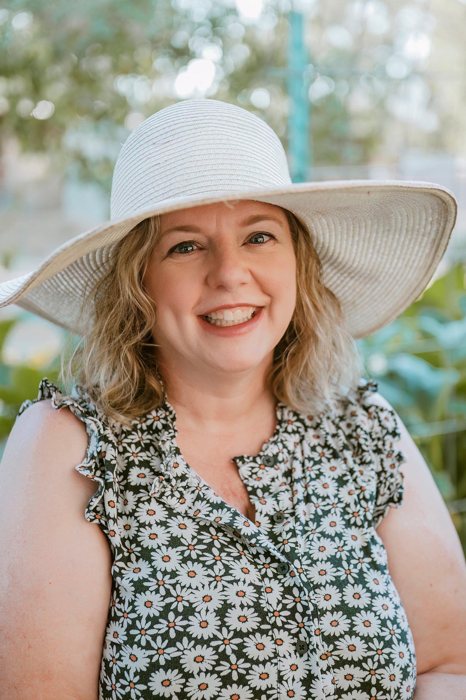 portrait of the owner in her garden, smiling and wearing a straw hat